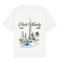 A white short-sleeve t-shirt with a graphic print of the Burj Khalifa in Dubai, featuring the text 'Club Ninety' and 'Classy Elegant'. The image includes promotional text overlays from 'The Gallery Drop' and 'Club Ninety'.
