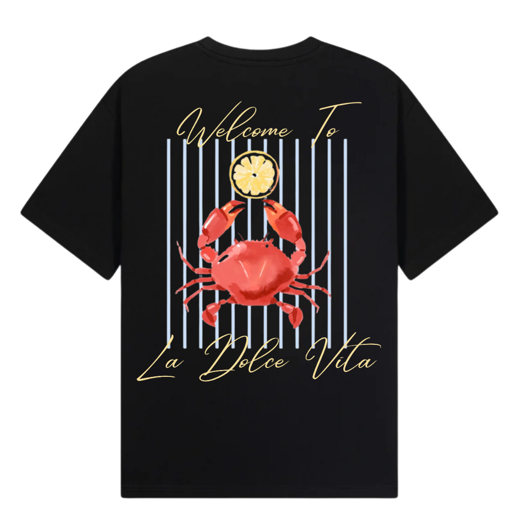 A black short-sleeve t-shirt with a graphic print on the front, featuring a red crab, a clock, vertical blue stripes, and gold script text reading 'Welcome To La Dolce Vita'. The image includes branding text overlays for 'THE GALLERY DROP', 'PEACE COLLECTIVE TEE', and 'CLUB NINETY' on a white background.