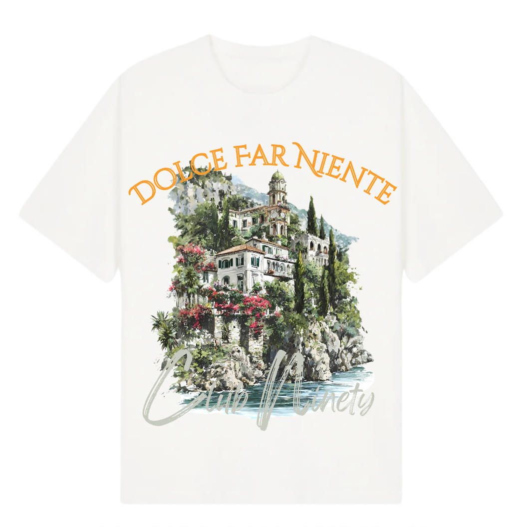 A white short-sleeve t-shirt featuring a colorful graphic print of a Mediterranean villa on a rocky island with the text 'DOLCE FAR NIENTE' in orange and 'Club Ninety' in gray script. The image includes promotional text overlays for 'The Gallery Drop' and 'Club Ninety'.