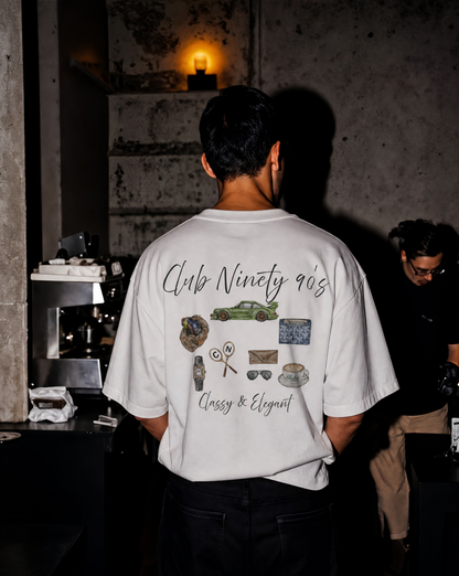 A man viewed from behind wearing a white t-shirt with a detailed graphic print on the back. The graphic features the text 'Club Ninety 90s' and 'Classy & Elegant' along with illustrations of a green car, sunglasses, a watch, and other vintage items.