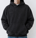 A man wearing a washed black pullover hoodie with 'CLOUDINARY' printed in gray on the left chest, paired with blue jeans, standing against a light gray studio background.