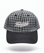 A baseball cap featuring a black and white plaid pattern on the crown with a solid black curved brim. The front of the cap has an embroidered white script logo reading 'Harvard'.